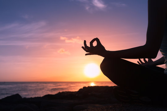 Hand of a woman meditating in a yoga pose on the beach.


