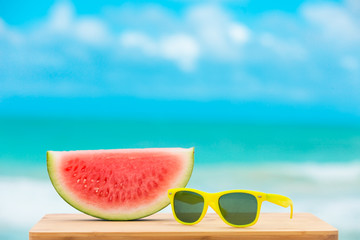 Happy summer holidays concept. Slice of watermelon and sunglasses against a beach background.  