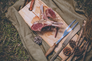 Raw rack of lamb put on a wood block with kitchen tools knife and fork on the grass floor
