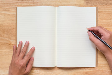 Top view of open notebook with two blank pages and hand hold pencil on wooden table