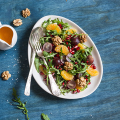 Delicious fruit salad. Grapes, tangerine, pomegranate and arugula fruit salad. On blue wooden background, top view. Flat lay
