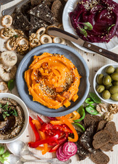 Vegetarian snack table. Pumpkin, beets hummus, beans and mushroom pate, vegetables, nuts, bread on a wooden table, top view. Flat lay