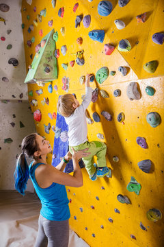 Young female bouldering instructor helping boy climb artificial wall