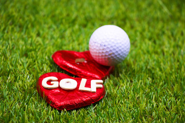 Golf ball with heart shape and golf lettering on green grass