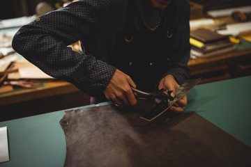 Craftswoman punching hole from leather punch machine in workshop