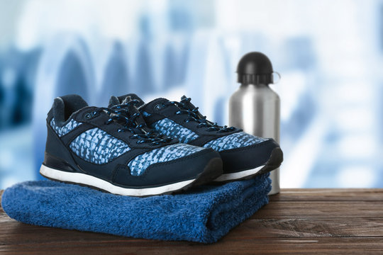 Sport Shoes, Towel And Bottle On Table Against Blurred Gym Interior Background