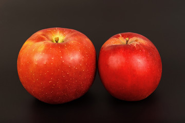 Two red ripe apples close up on a black background.