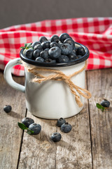 Fresh blueberries in enameled cup and red towel, rustic background, selective focus