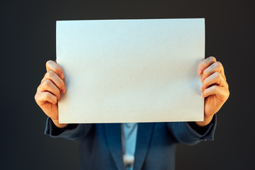 Businesswoman covering face with blank paper as copy space