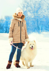 Woman owner and white Samoyed dog on leash walking in winter par