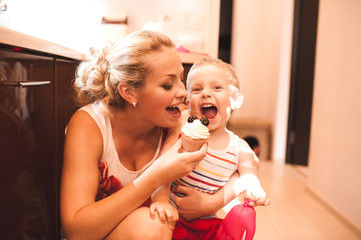 Smiling woman holding child boy 3-4 year old having fun with cupcake at kitchen. Motherhood.