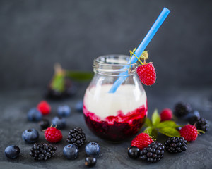 Yogurt with fresh berries fruit on dark stone background.
