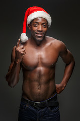 Muscular black shirtless young man in Santa Claus hat - obrazy, fototapety, plakaty