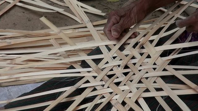 Basket Weaving Lady. An ederly Asian woman weaves baskets for sale in the local market. A close-up of her hands as she works.