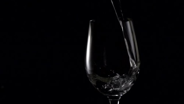 slow motion,pouring water into glass of water on black background. 