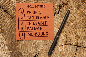 Conceptual SMART Goals acronym on piece of wood with pen (Specific, Measurable, Achievable, Realistic, Time-bound) 