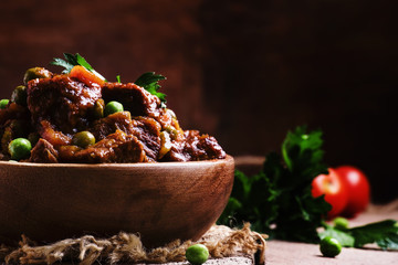 Ragout with beef, carrots, green peas and tomatoes, old wooden b