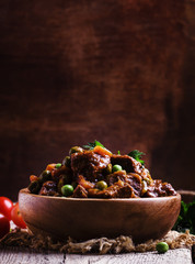 Ragout with beef, carrots, green peas and tomatoes, old wooden b