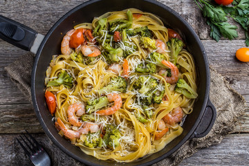 Pasta linguine with shrimps and broccoli in dripping pan on wooden background.