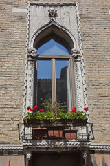 Window with small balcony, iron fence and green plants in pots against brick wall, Venice