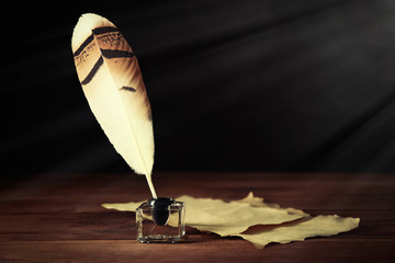 Feather pen with inkwell and blank paper on dark background
