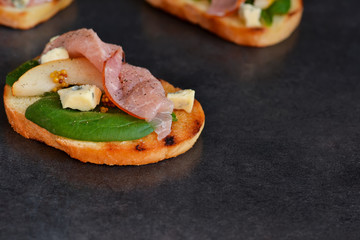 Toast with sauce, ham, pear and blue cheese on a black background