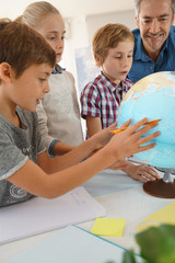 Fototapeta premium Teacher with kids in geography class looking at globe