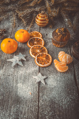 Xmas or new year composition with holiday decoration - Homemade cupcakes, sliced dried oranges and mandarin on wooden background with spruce twigs and christmas toy. Christmas card. Space for text