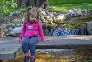 Cute little girl sitting on the old wooden bridge looking at the water in Japanese garden on the beautiful sunny day © bojandimic