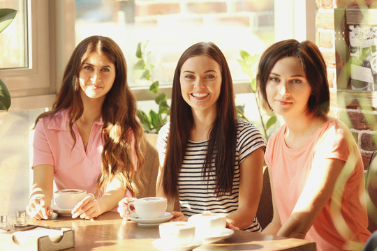 Cheerful young women drinking coffee in cafe on sunny day