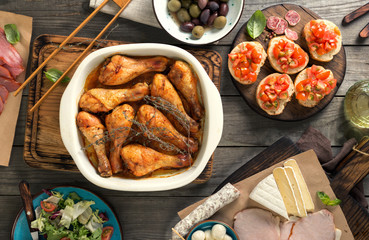 Baked chicken legs with variety of snacks on wooden table