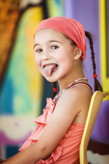 little girl shows tongue sitting on a chair