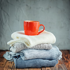 Sweaters Closeup, Stack of knitted winter clothes with red mug on wooden background.