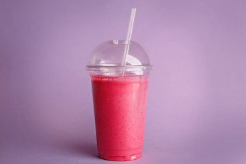 Delicious strawberry milkshake in plastic cup on purple background