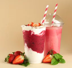 Photo sur Plexiglas Milk-shake Délicieux cocktails aux fraises dans des gobelets en plastique sur fond beige