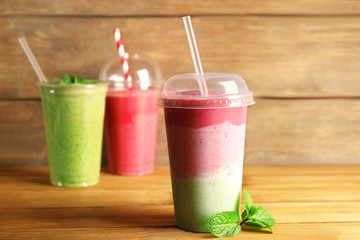Tasty fruit cocktails in plastic cups on wooden background