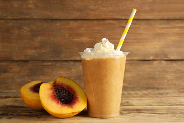 Tasty peach milkshake with cream in plastic cup on wooden background