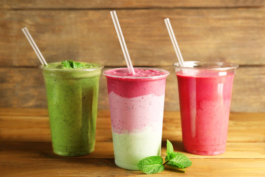 Tasty fruit cocktails in plastic cups on wooden background