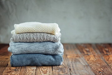 Stack of knitted winter clothes on wooden background, sweaters, space for text. Toning image