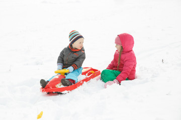 Fototapeta na wymiar Brother and sister sledding in a snowy winter landscape