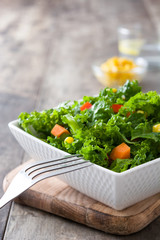 Kale salad in white bowl on wooden table