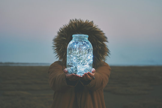 Girl is holding fairy lights in a jar on winter dry landscape - Powered by Adobe