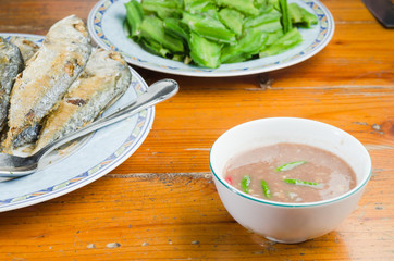a cup of shrimp paste serving with fried mackerel and vegetable on wood table