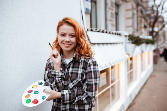 Cheerful young lady painter with red hair walking on street
