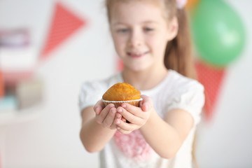 Little girl holding tasty muffin on blurred background, close up