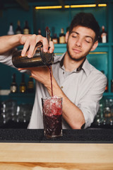 Young handsome barman pouring cocktail drink into glass