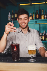 Young handsome barman pouring cocktail drink into glass
