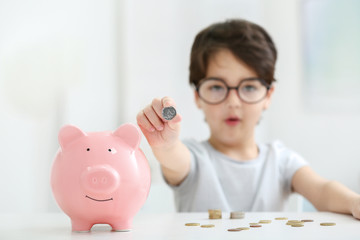 Portrait of cute little boy in glasses with a piggy bank on blurred background