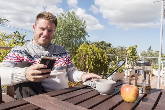 Happy man having breakfast with technology in the garden