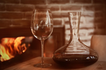 Decanter and wine glass on wooden table against fireplace